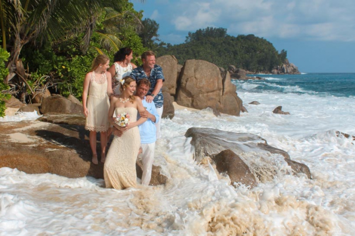 This photo shows exited wedding group at the beach with wave coming in
